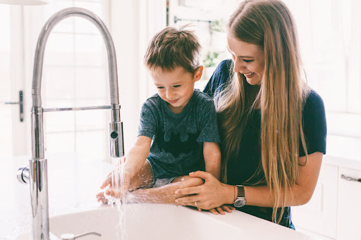 A mom and child using a kitchen sink faucet.