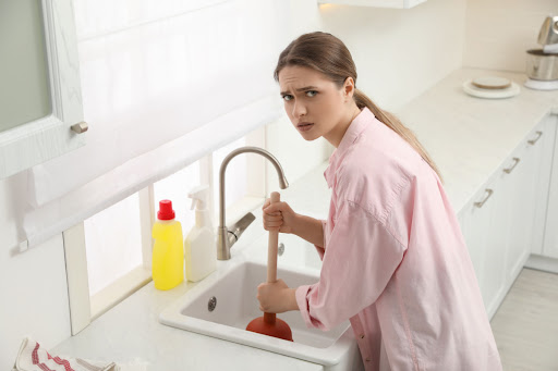 A woman plunging a clogged sink. She has a worried expression on her face.