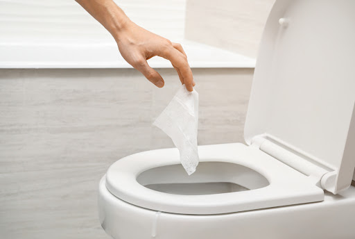 Hand holding "flushable" wipe into toilet drain.
