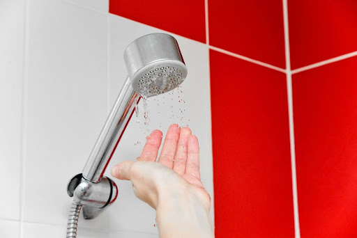 A hand feeling the water as it flows from a shower head.