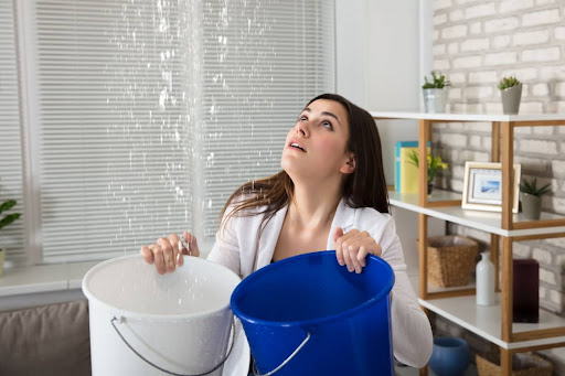 A woman collecting water leaking from a ceiling with two buckets.